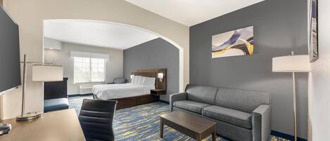 Una habitación de hotel con una cama, un sofá, una mesa de centro, un escritorio y una lámpara.