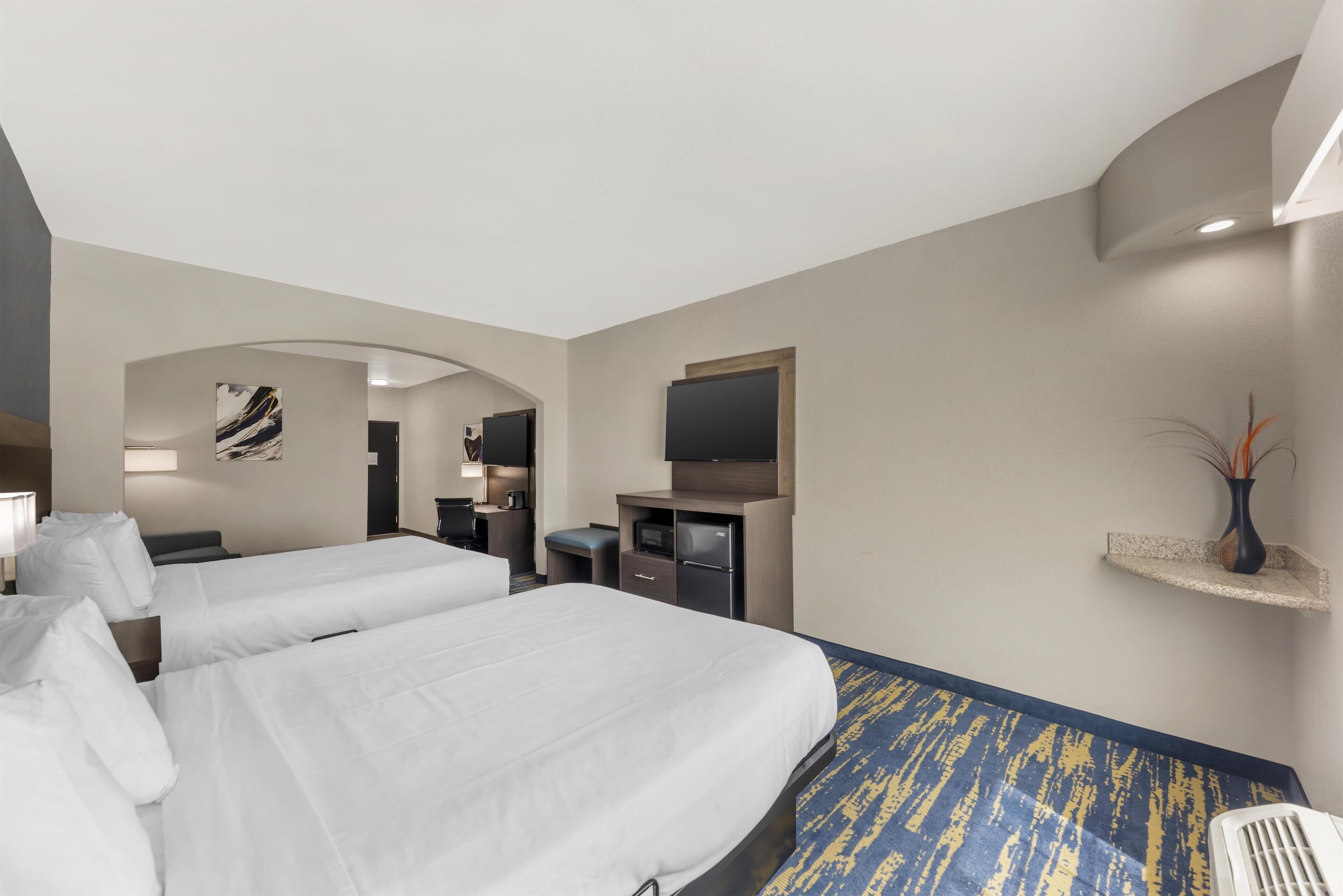 Una habitación de hotel con dos camas, un escritorio, un televisor y un pequeño rincón de descanso.