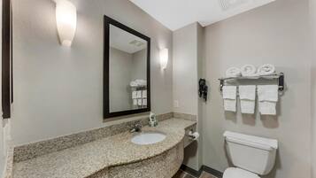 A bathroom with a granite countertop sink, a white toilet, a mirror, and a towel rack with towels.
