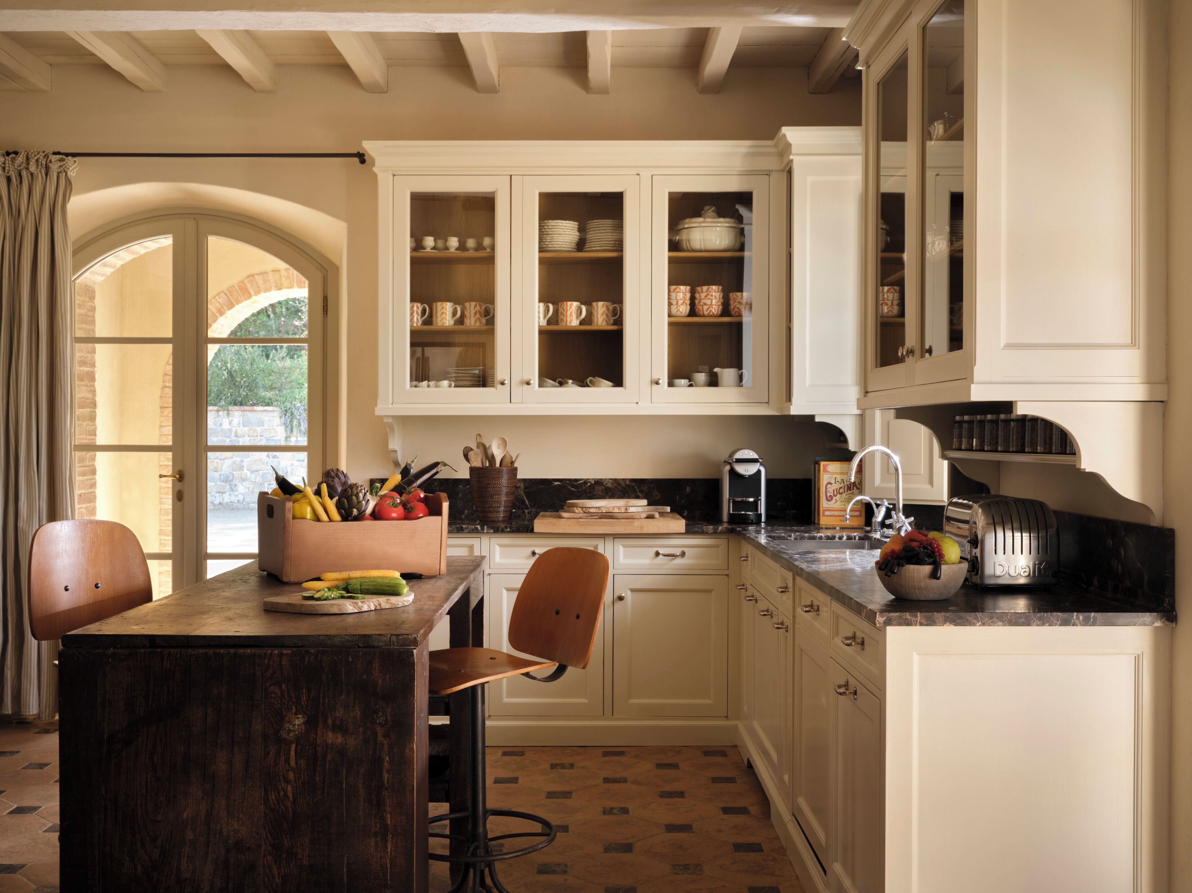A kitchen with white cabinets, a wooden table, and a fruit bowl.