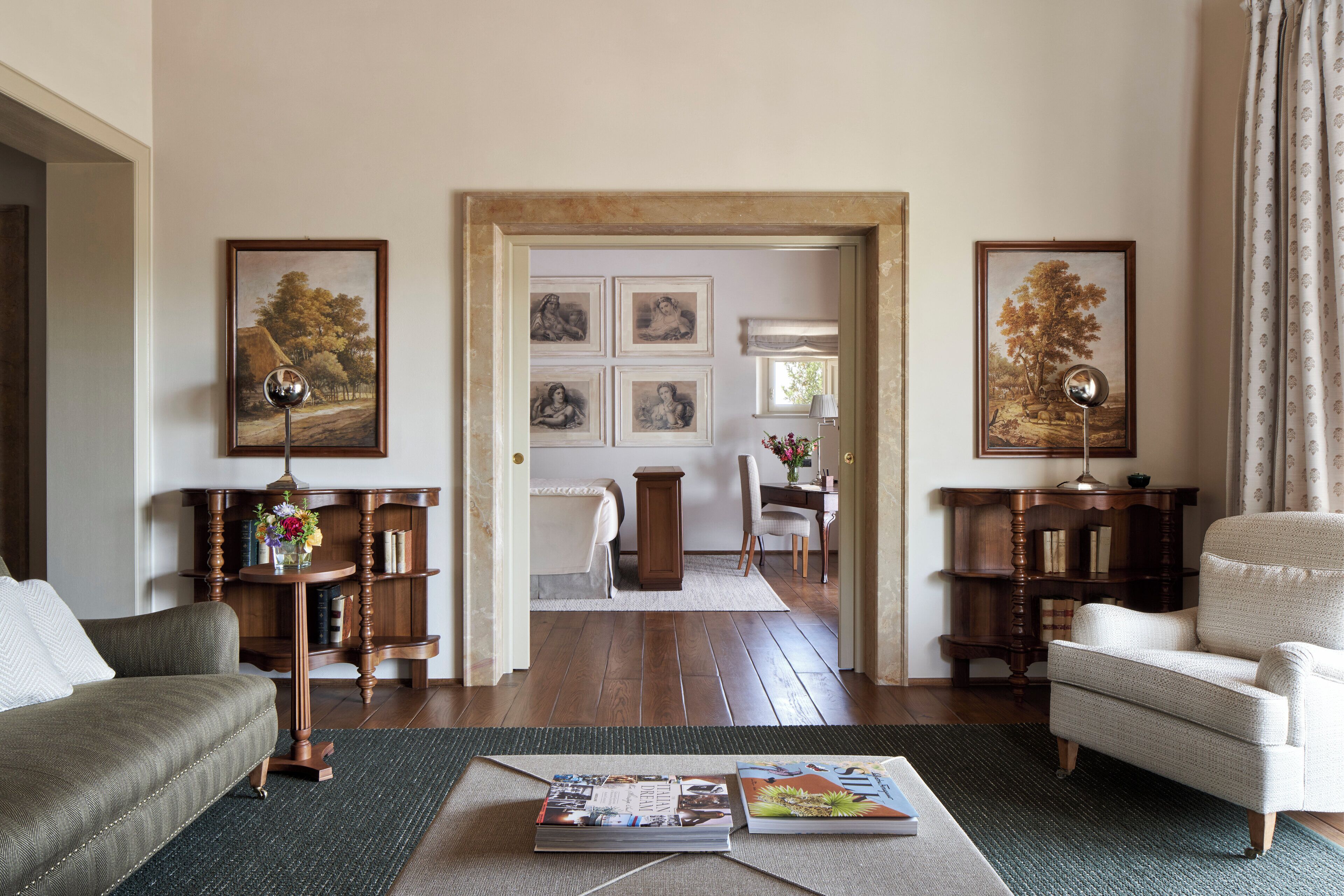 Una sala de estar con sofá, sillón y mesa de centro, suelo de madera y cuadros en las paredes.