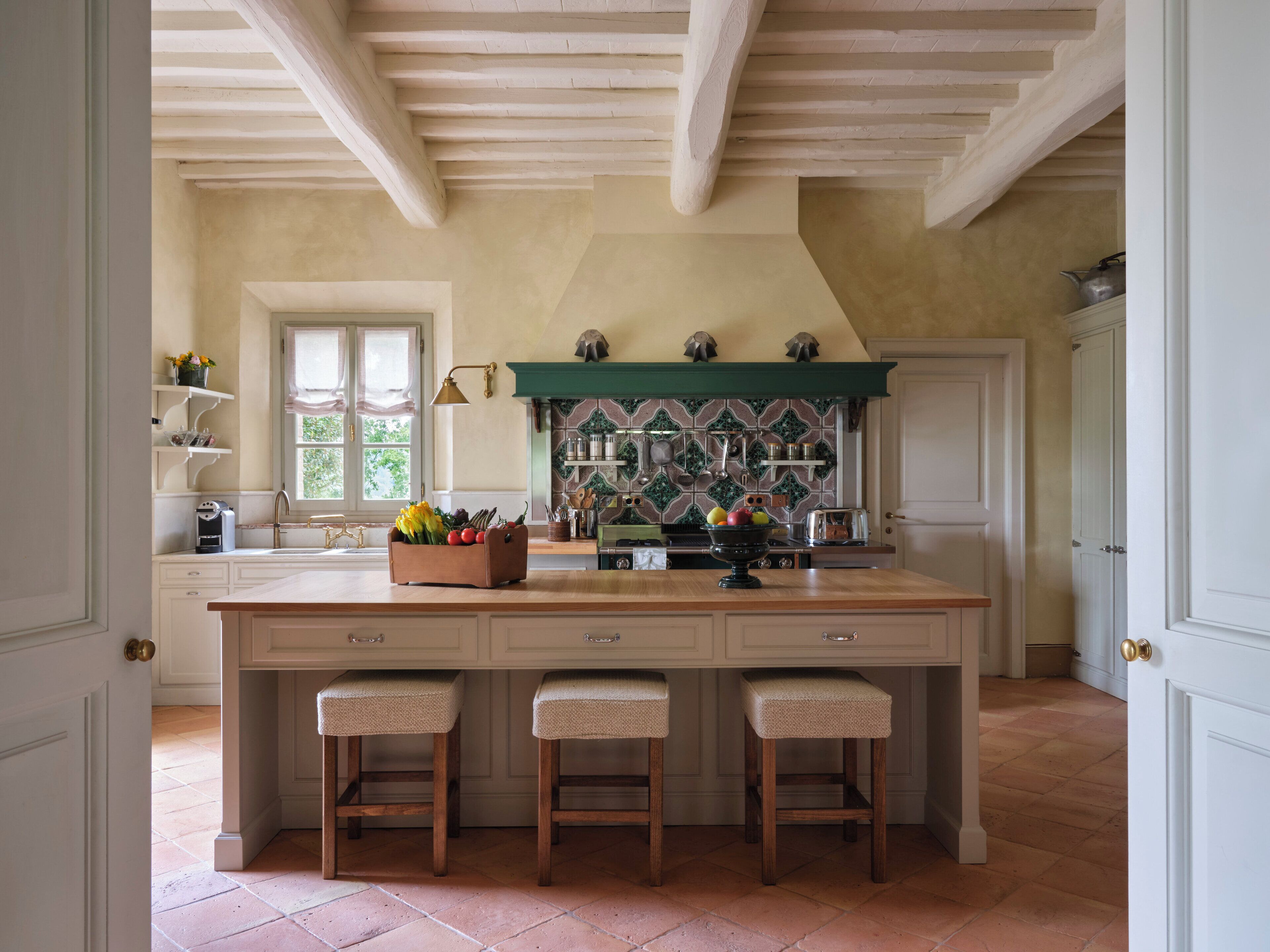 A spacious kitchen with a large island, wooden stools, and a tiled backsplash.