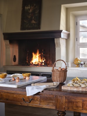 Una cocina con chimenea, una mesa de madera con ingredientes para hornear y una cesta de huevos.