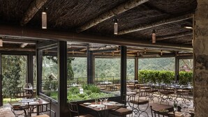 Un área de comedor al aire libre con mesas y sillas, ventanas amplias y vistas del paisaje circundante.