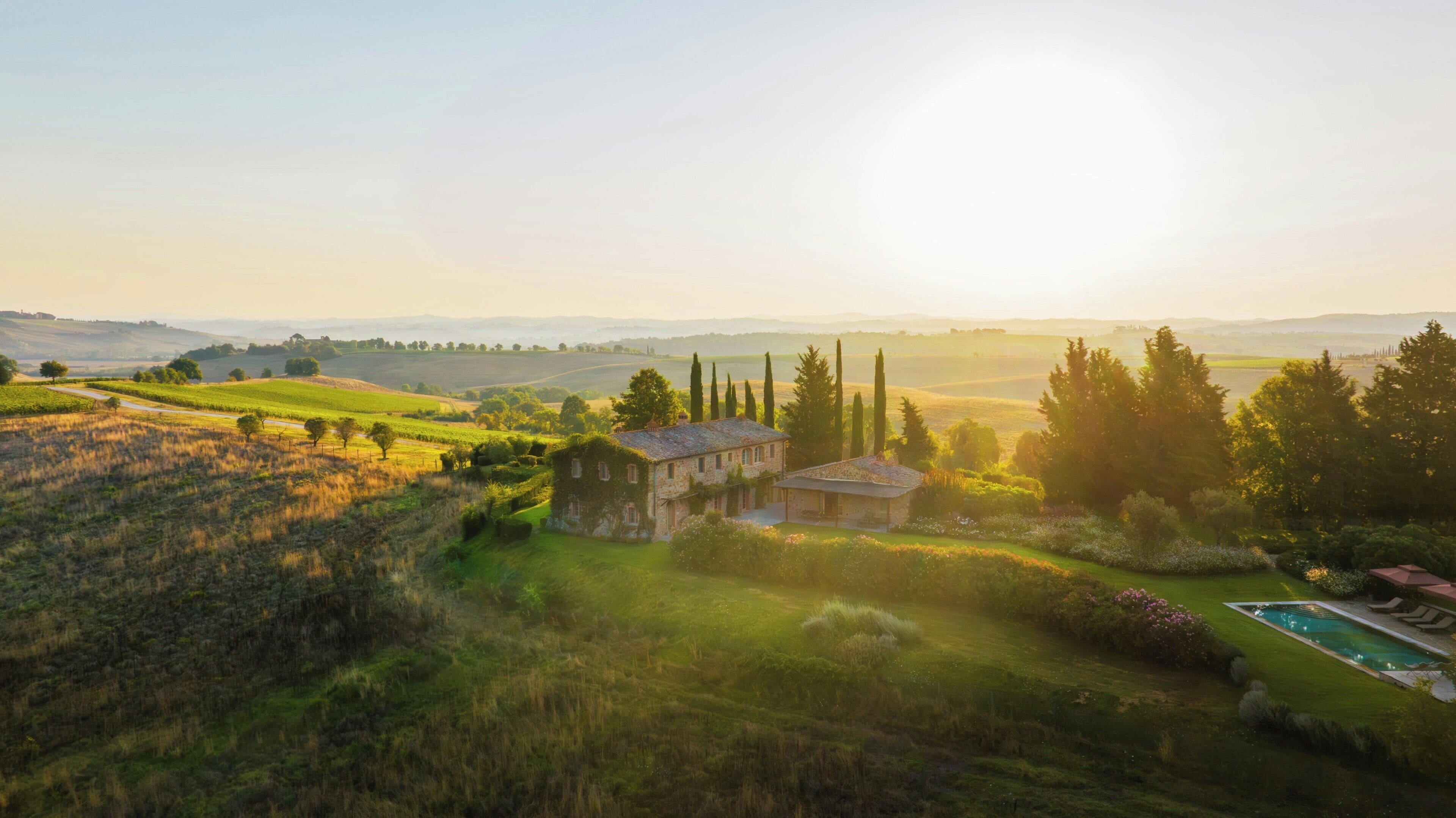 A rural landscape with a stone house, a swimming pool, and rolling hills in the background.