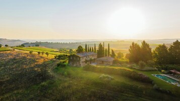 A rural landscape with a stone house, a swimming pool, and rolling hills in the background.