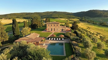 Una villa de piedra con piscina, rodeada de exuberante vegetación y colinas.