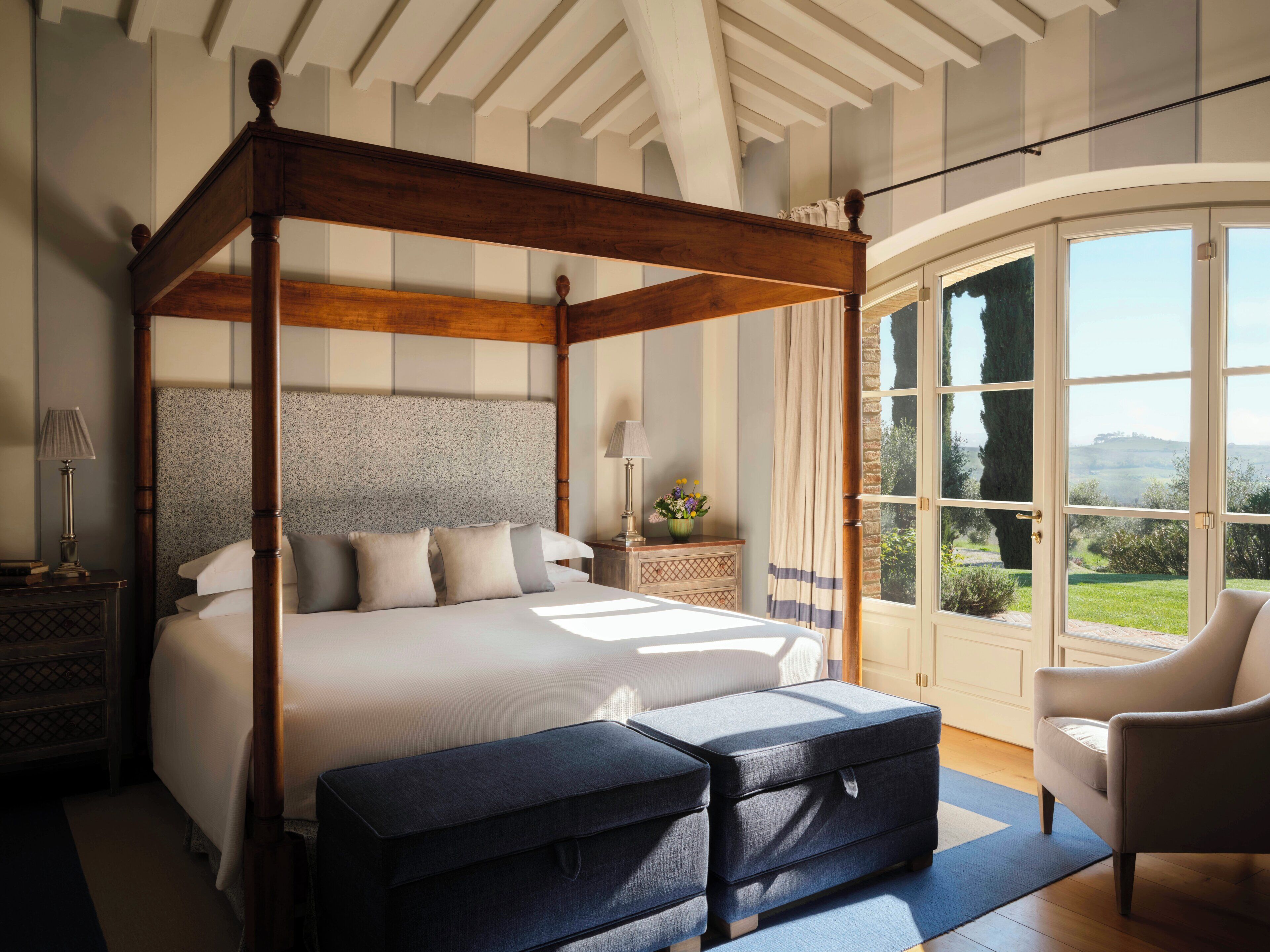 Una cama con dosel y cabecera, una zona de estar con una silla, y vistas del exterior a través de amplios ventanales.