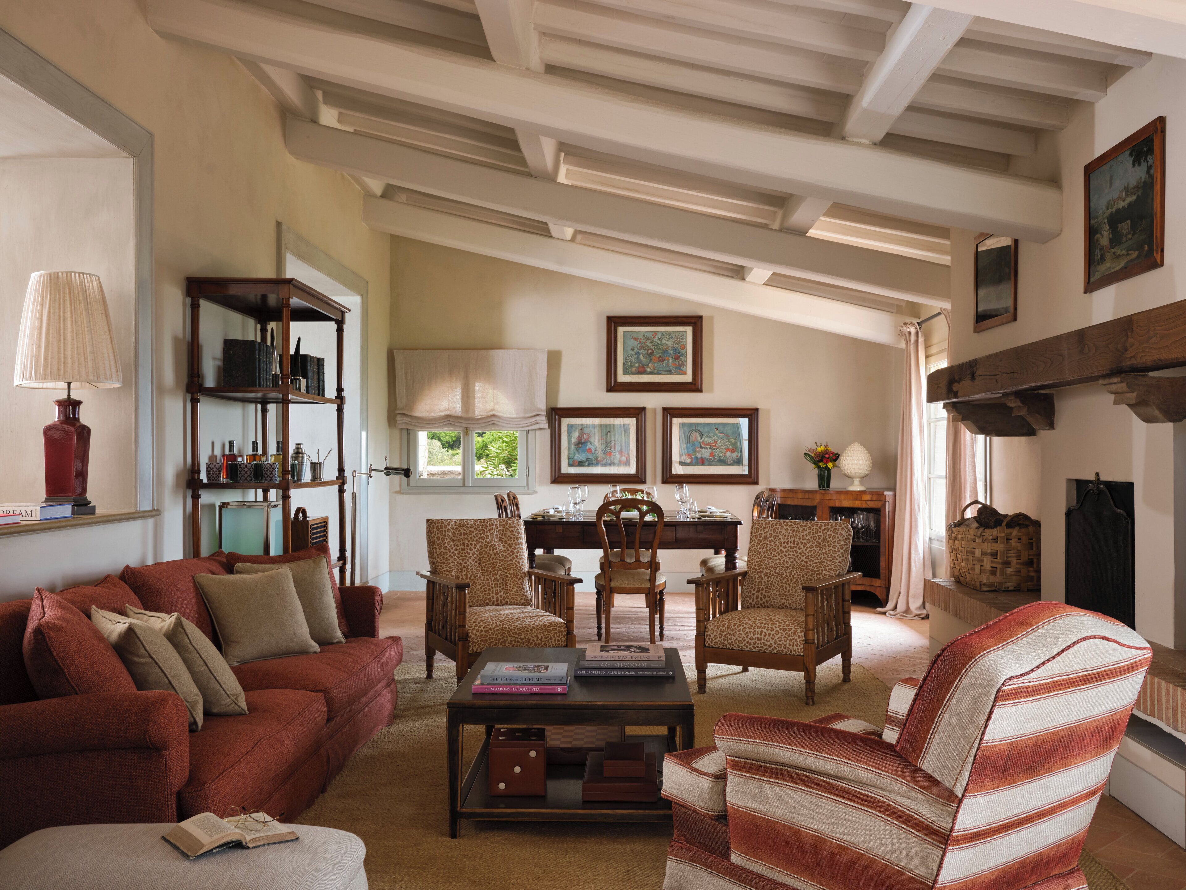 A cozy living room with a red sofa, a striped armchair, and a coffee table with books. There is a bookshelf, a fireplace, and framed artwork on the wall.