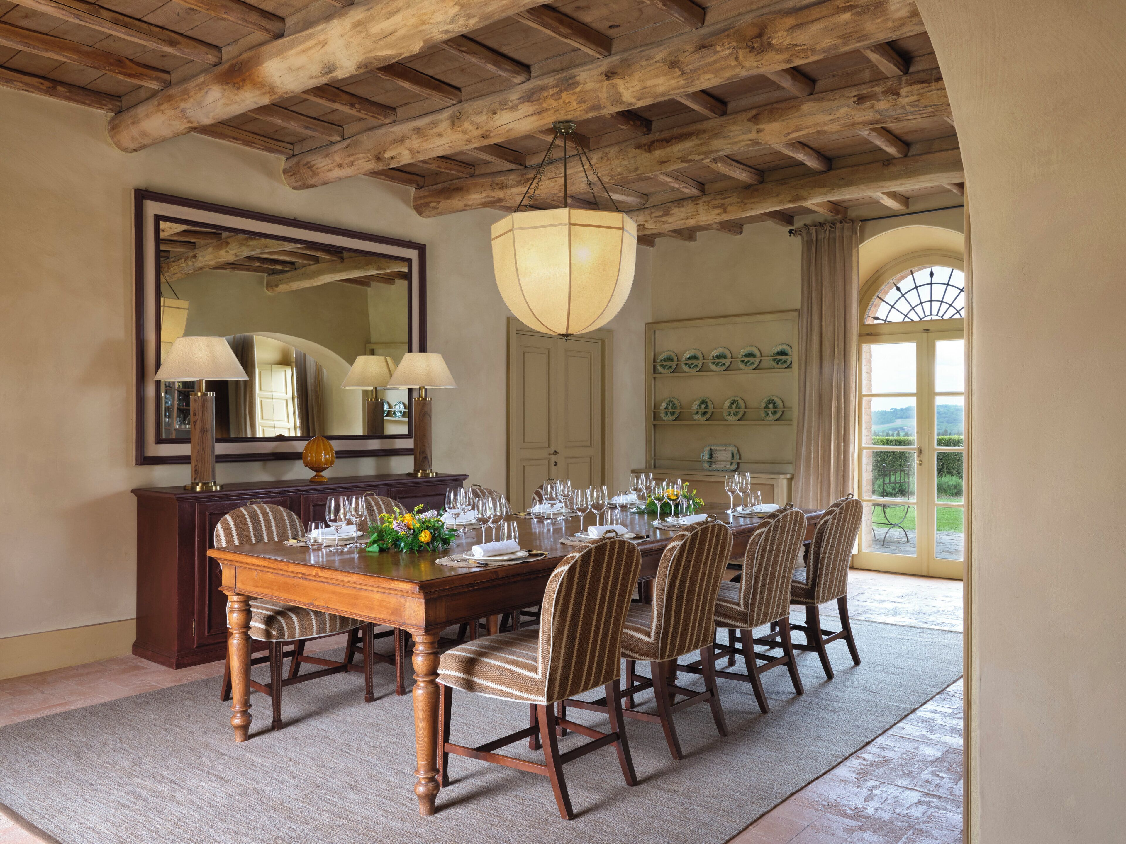 Comedor con mesa de madera dispuesta para seis comensales, rodeada por seis sillas, un espejo grande y una araña.