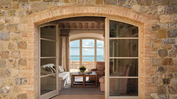 Una habitación con paredes de piedra, un arco grande en la entrada, un sofá, una mesa con un florero, y vistas al paisaje.