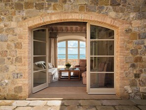Una habitación con paredes de piedra, un arco grande en la entrada, un sofá, una mesa con un florero, y vistas al paisaje.