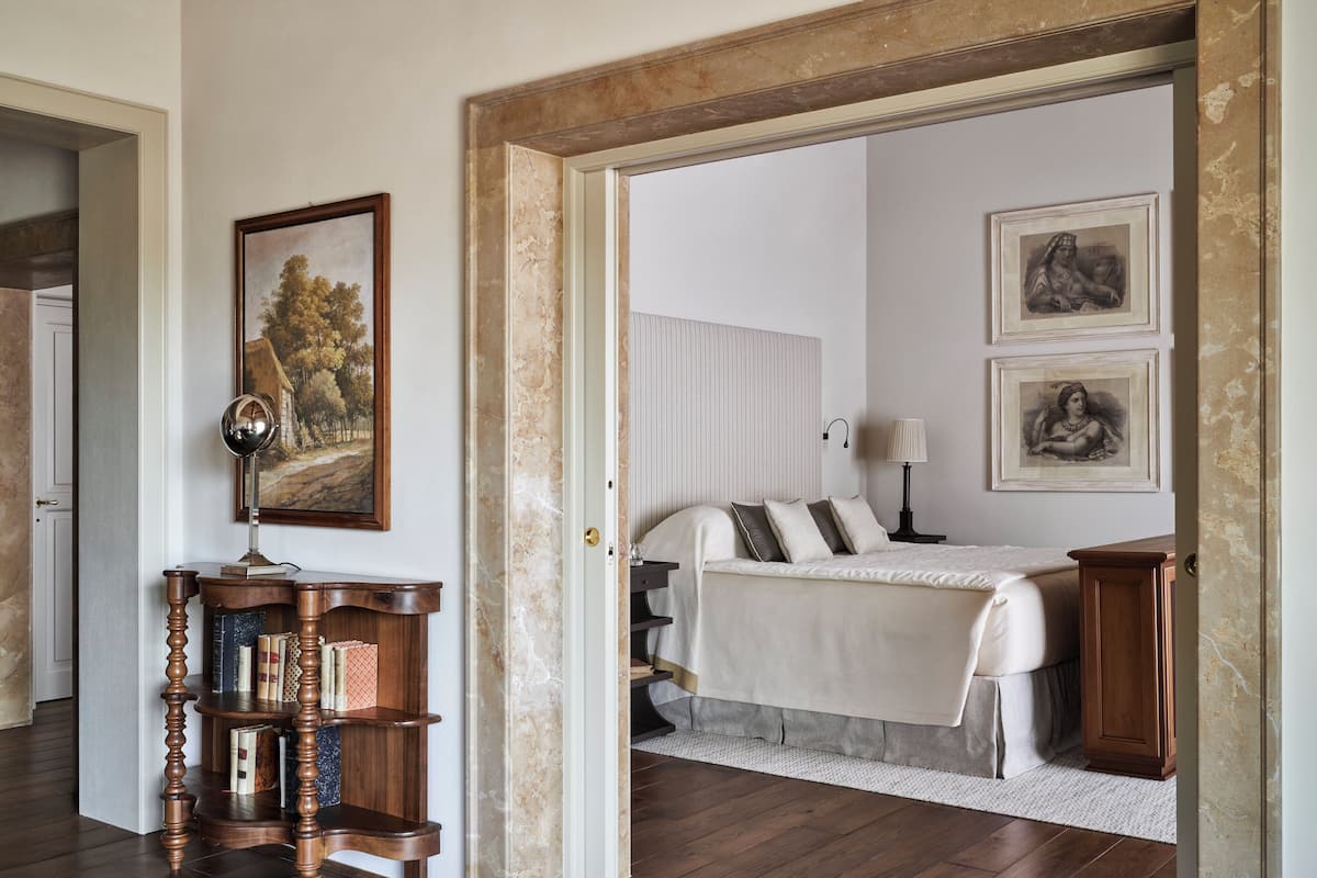 Un dormitorio con cama, mesitas de noche, estantería y cuadros en la pared.