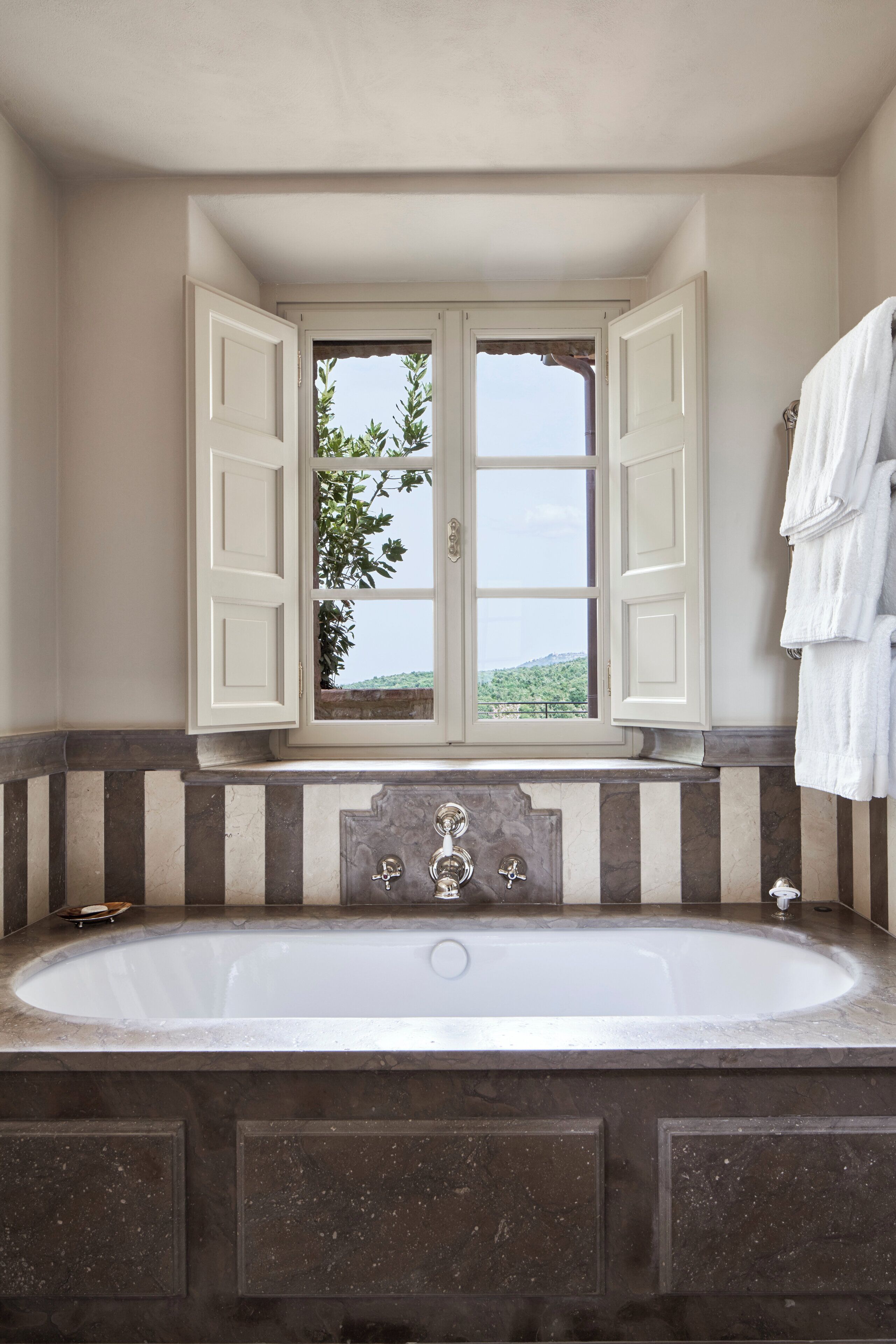 Un baño con una bañera grande, una ventana con contraventanas abiertas y un perchero para toallas.