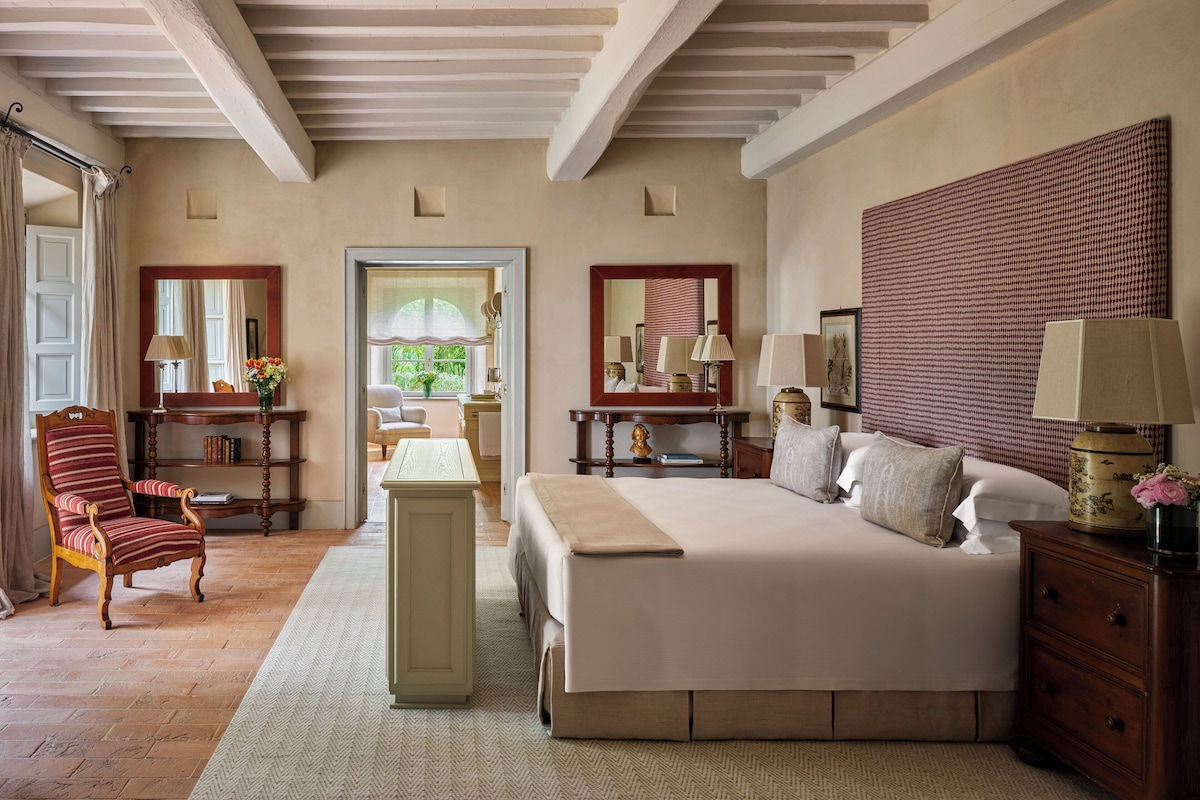 A spacious bedroom with a large bed, a wooden chair, a desk, and a mirror.