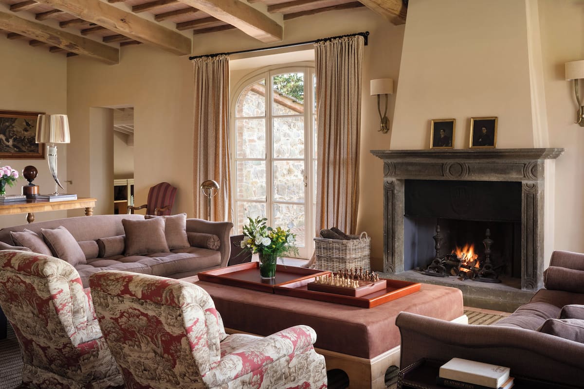 Una sala de estar acogedora con chimenea, un ventanal con cortinas y un tablero de ajedrez sobre una mesa de centro.