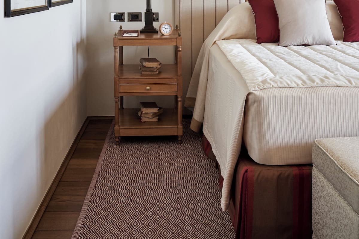 Un dormitorio con cama, mesita de noche, lámpara, cuadros enmarcados y alfombra estampada.