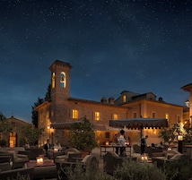Un edificio histórico con un campanario, asientos al aire libre y un cielo estrellado.
