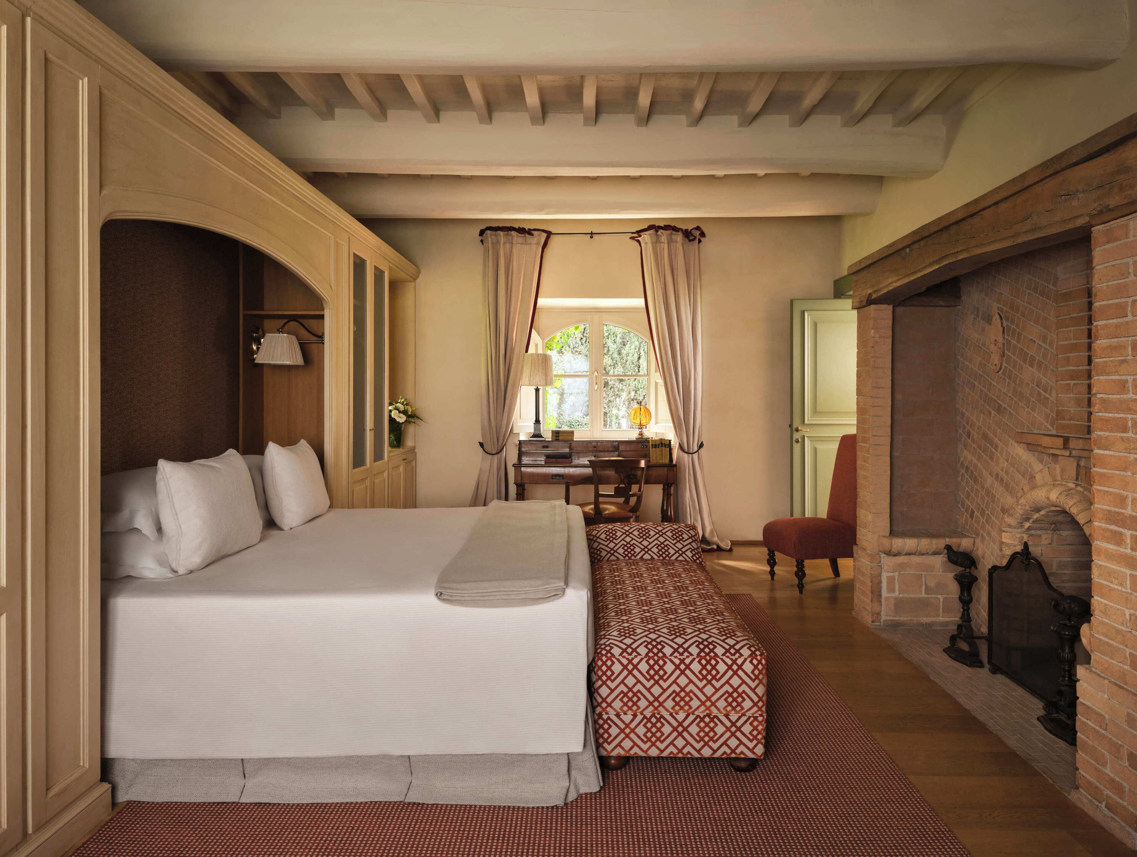 A bedroom with a large bed, a desk, and a fireplace.
