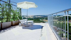 A balcony with a white umbrella, white chairs, and a view of a valley. - Hotel Sirolo (Sirolo)