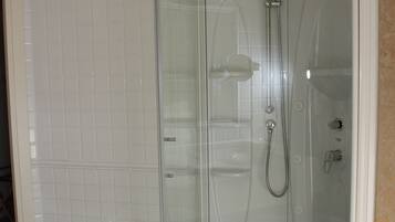 Une salle de bain moderne dotée d’une douche à l’italienne avec parois en verre, d’une baignoire sur pieds et de murs recouverts de carreaux blancs.