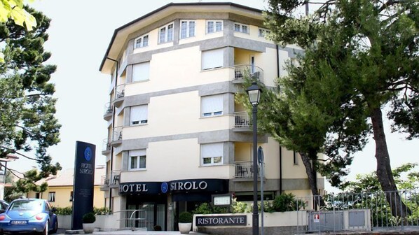 A multi-story hotel with balconies, a sign for a restaurant, and a car parked in front. - Hotel Sirolo (Sirolo)