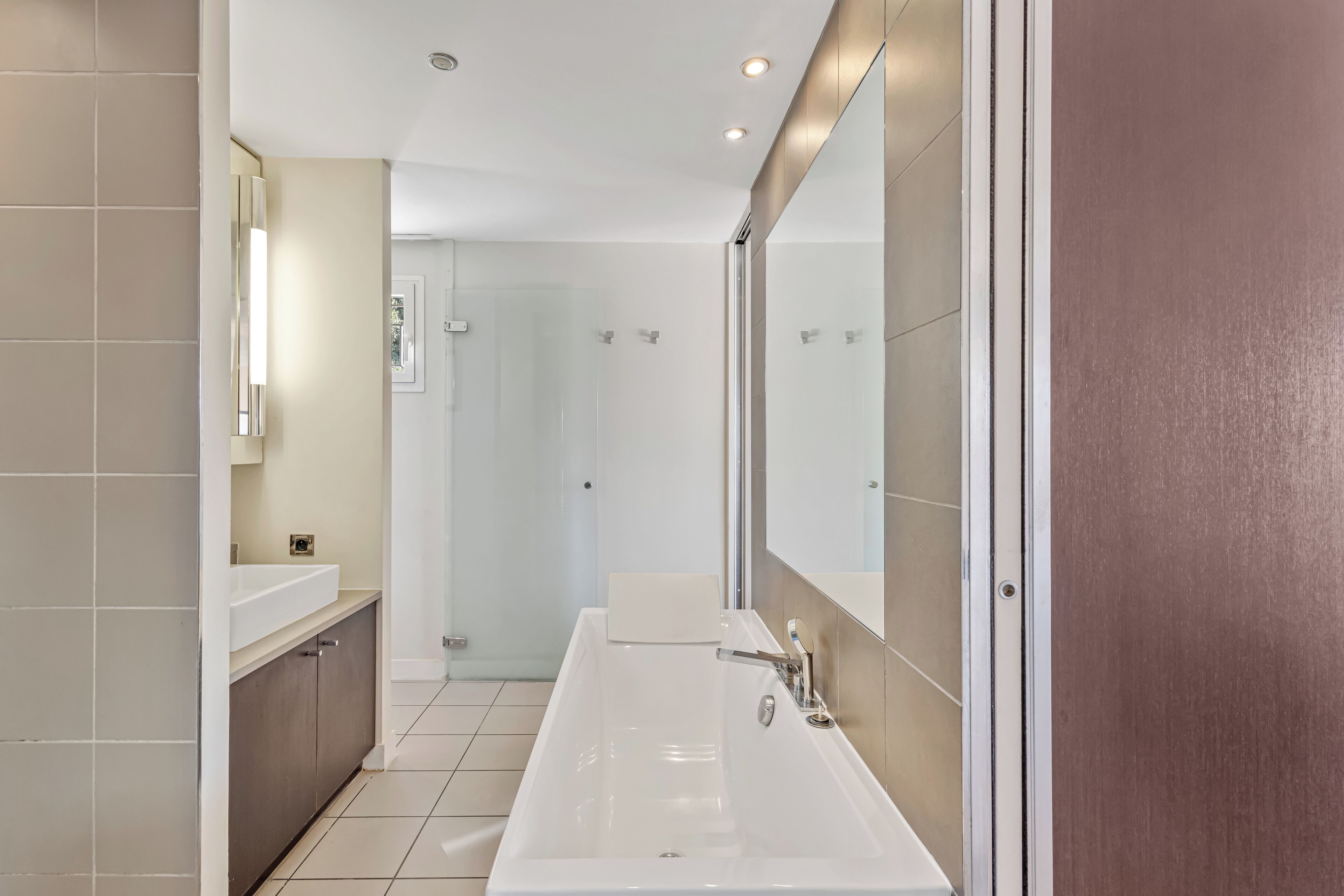A modern bathroom with a large mirror, two sinks, and a shower area.