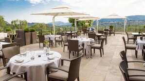 Een terras met ronde tafels en stoelen, afgedekt met parasols, met een prachtig uitzicht op de achtergrond.
