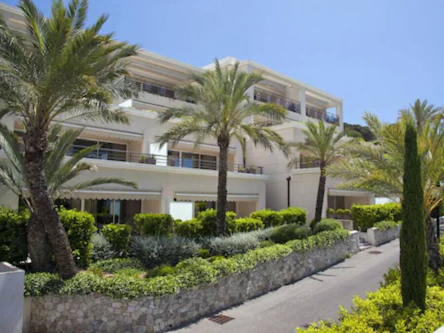 Un hotel moderno con una estructura de dos pisos, un camino bordeado de piedra y palmeras.