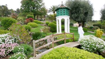 A garden with a wooden bridge, a white gazebo, and various flowering plants.
