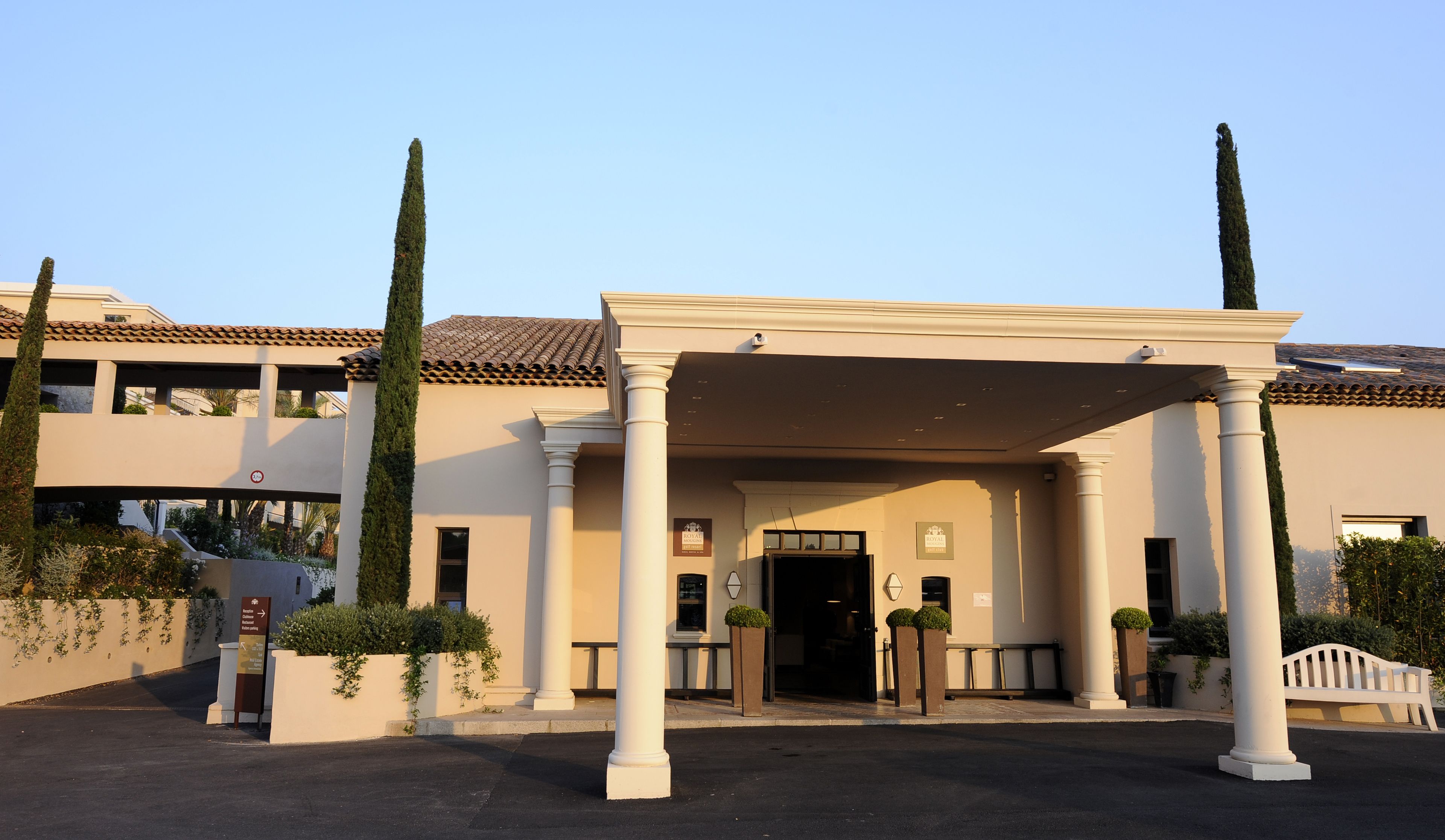 Entrada de hotel con un camino cubierto, columnas y un letrero que indica zona de estacionamiento.