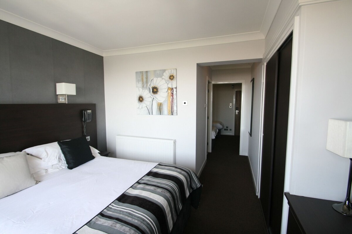 A hotel room with a large bed, a bedside table, a lamp, and a painting on the wall.