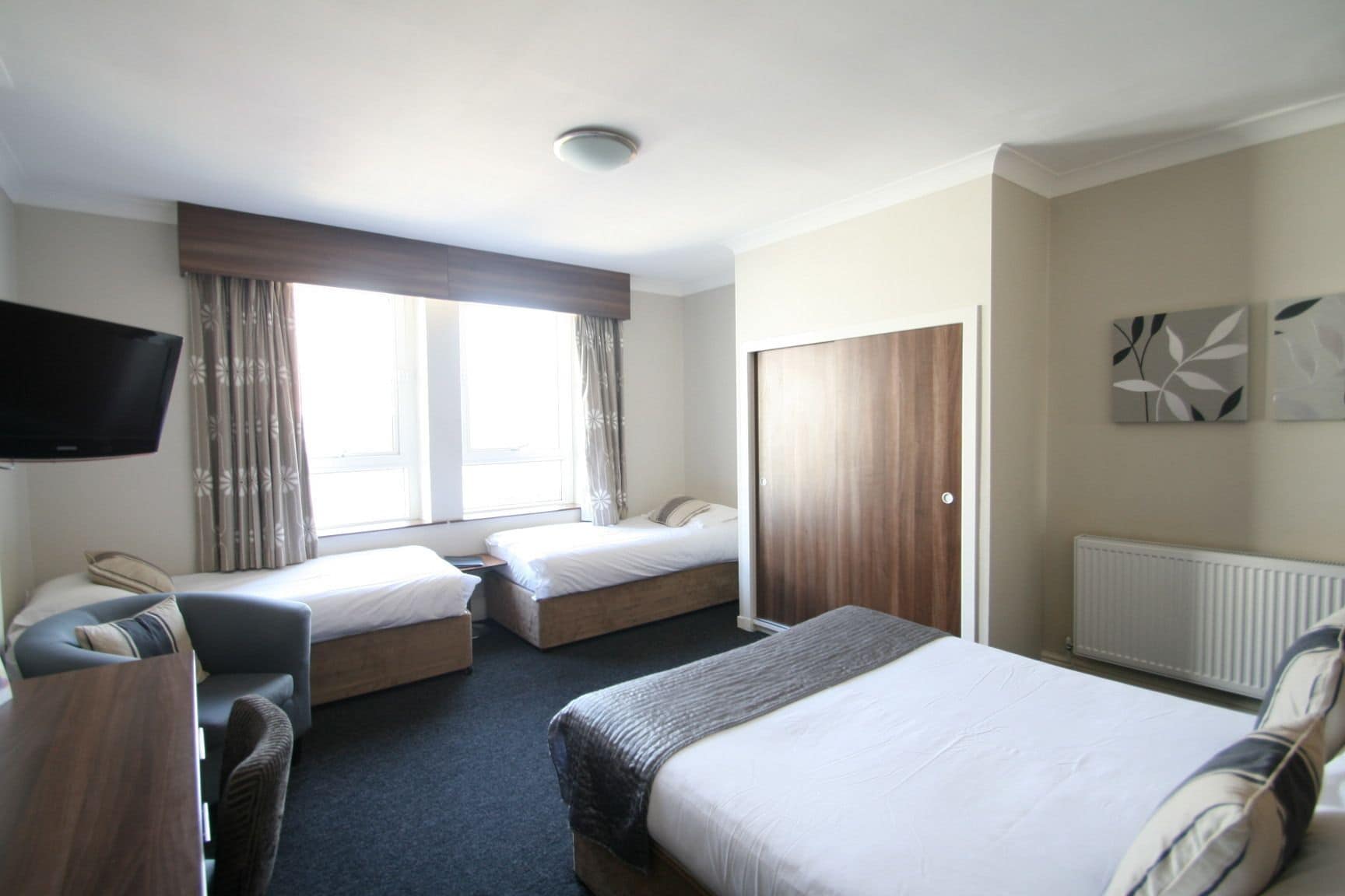 Une chambre d’hôtel avec deux lits simples, un canapé, une télévision et une fenêtre avec des rideaux.