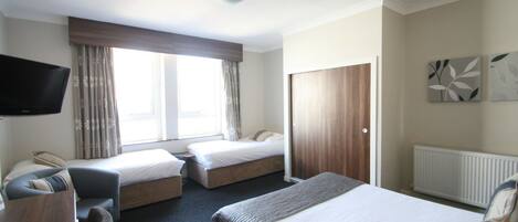 Une chambre d’hôtel avec deux lits simples, un canapé, une télévision et une fenêtre avec des rideaux.