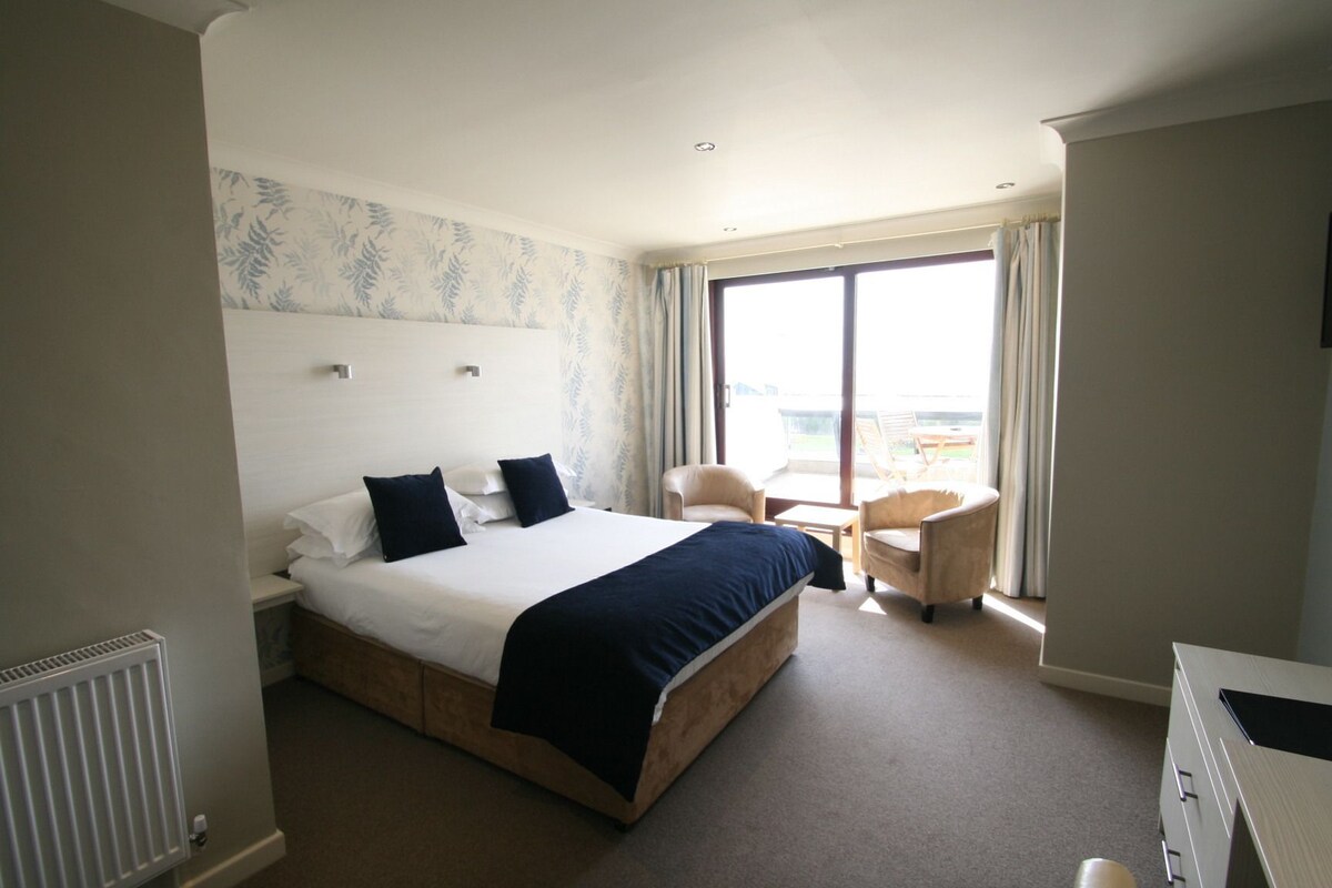 A hotel room with a large bed, a desk, a chair, and a view of the outdoors.