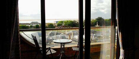 A balcony with a table and chairs, overlooking a parking area and a distant building.