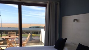 A hotel room with a large bed, a view of the beach, and a balcony with a table and chairs. - Dalmeny Resort Hotel (Lytham St. Anne's)