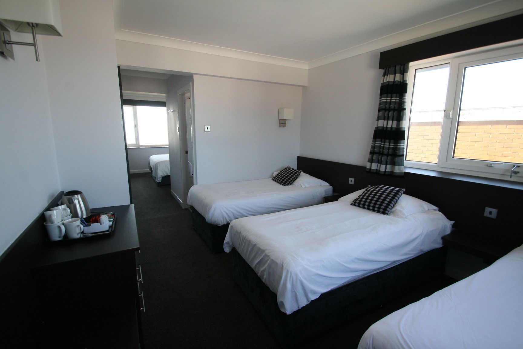 A hotel room with two single beds, a desk with a tray of breakfast items, a window with curtains, and a view of the outside.