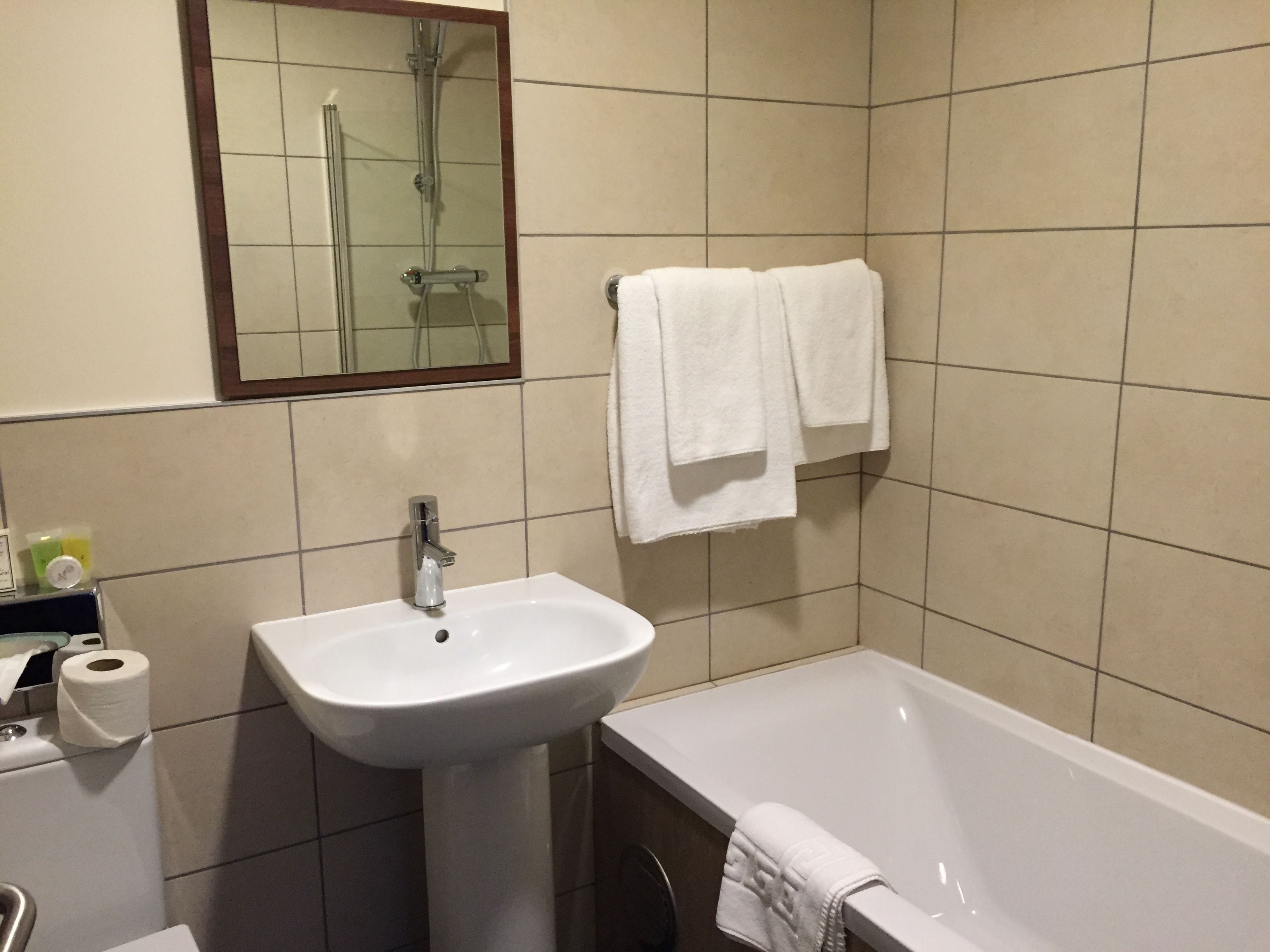 Une salle de bain avec un lavabo, un miroir, une baignoire et deux serviettes blanches accrochées au mur.