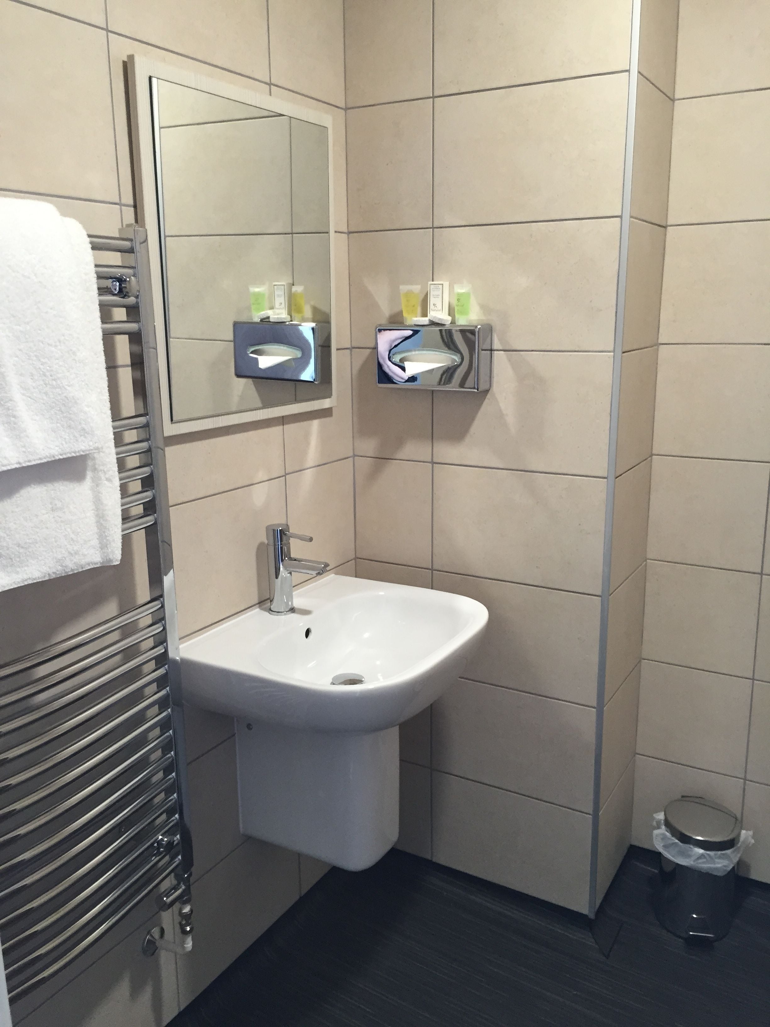 A bathroom with a white sink, a towel rack, a mirror, and a trash bin.