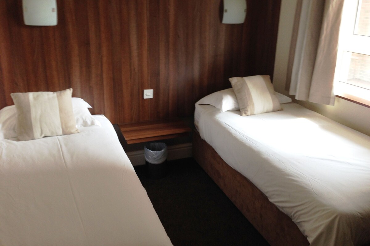 A hotel room with two beds, wooden paneling on the walls, and a window with curtains.