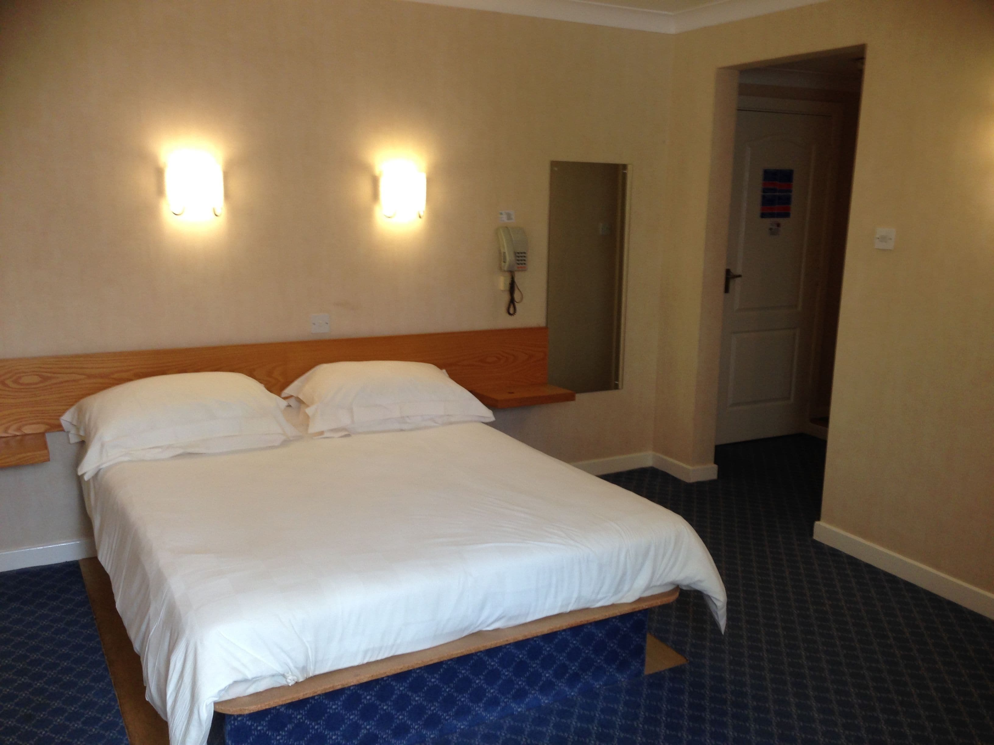 Habitación de hotel con una cama, dos lámparas de pared, un teléfono y una puerta.
