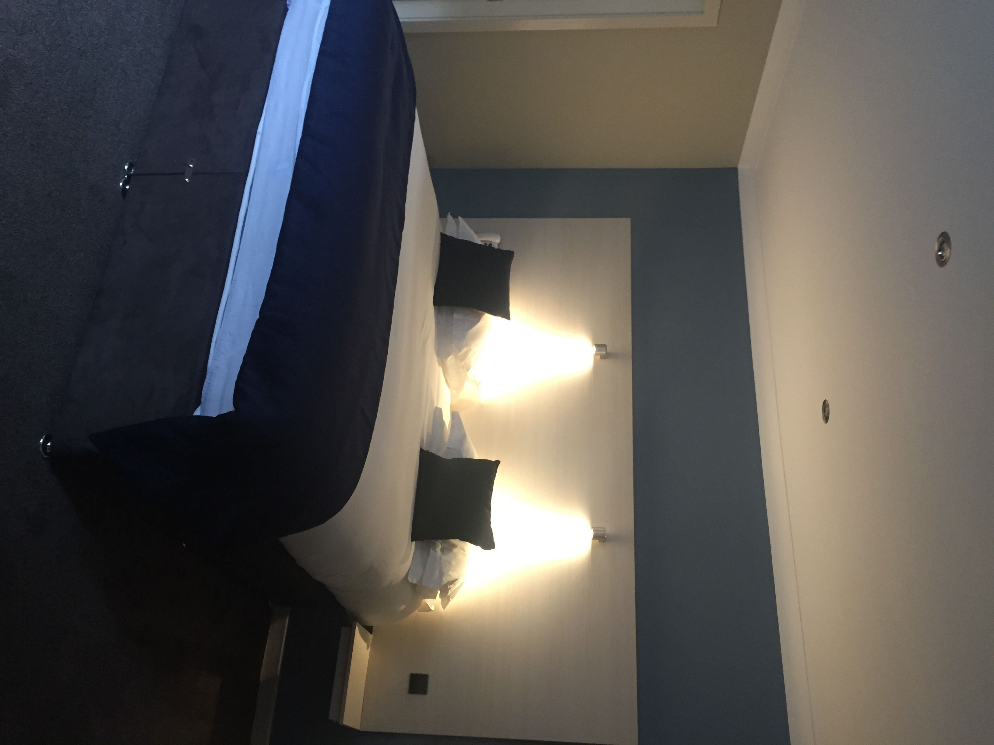 A hotel room with a bed, two wall-mounted lights, and a door.