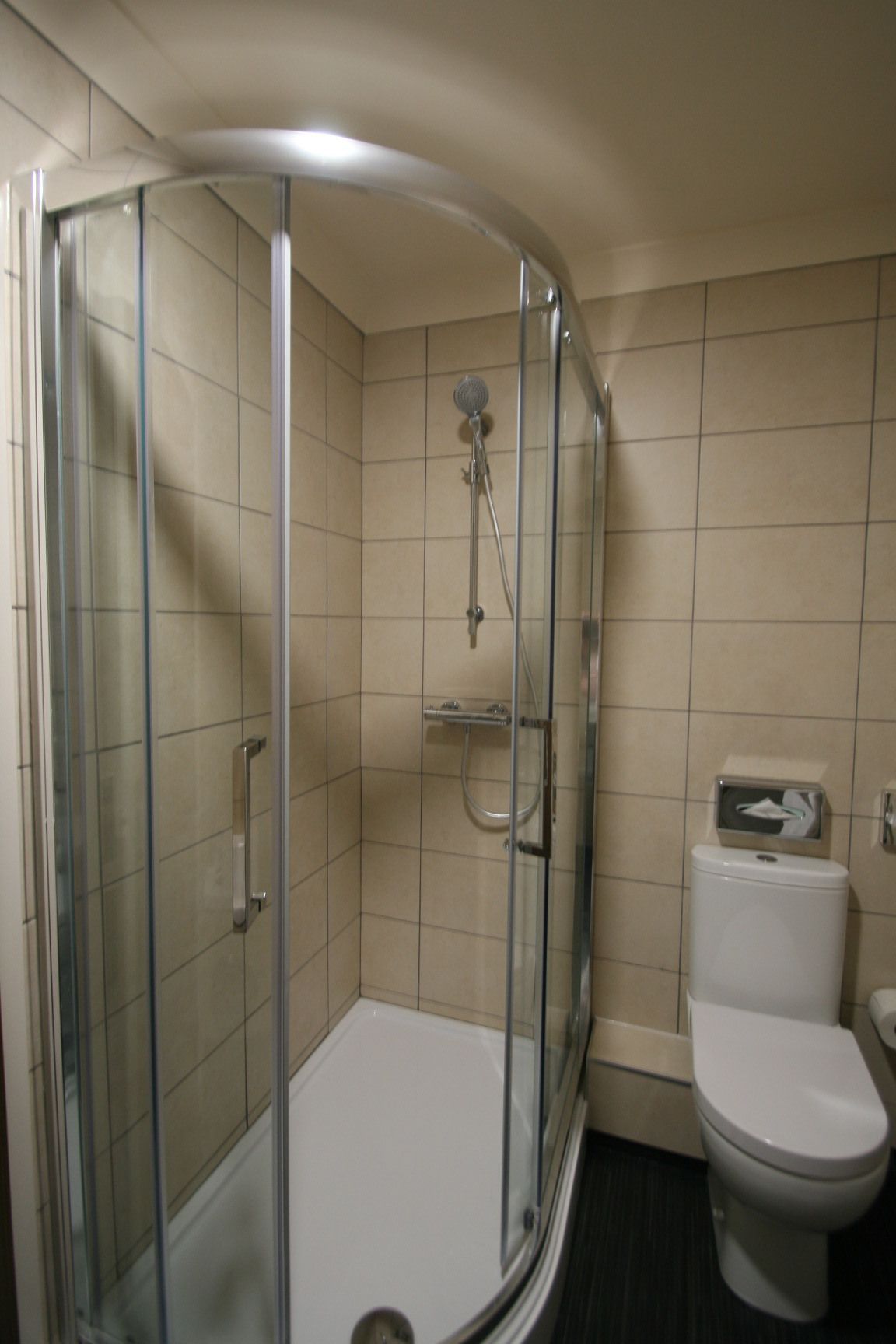 Un baño con ducha de vidrio, inodoro y secador de manos.