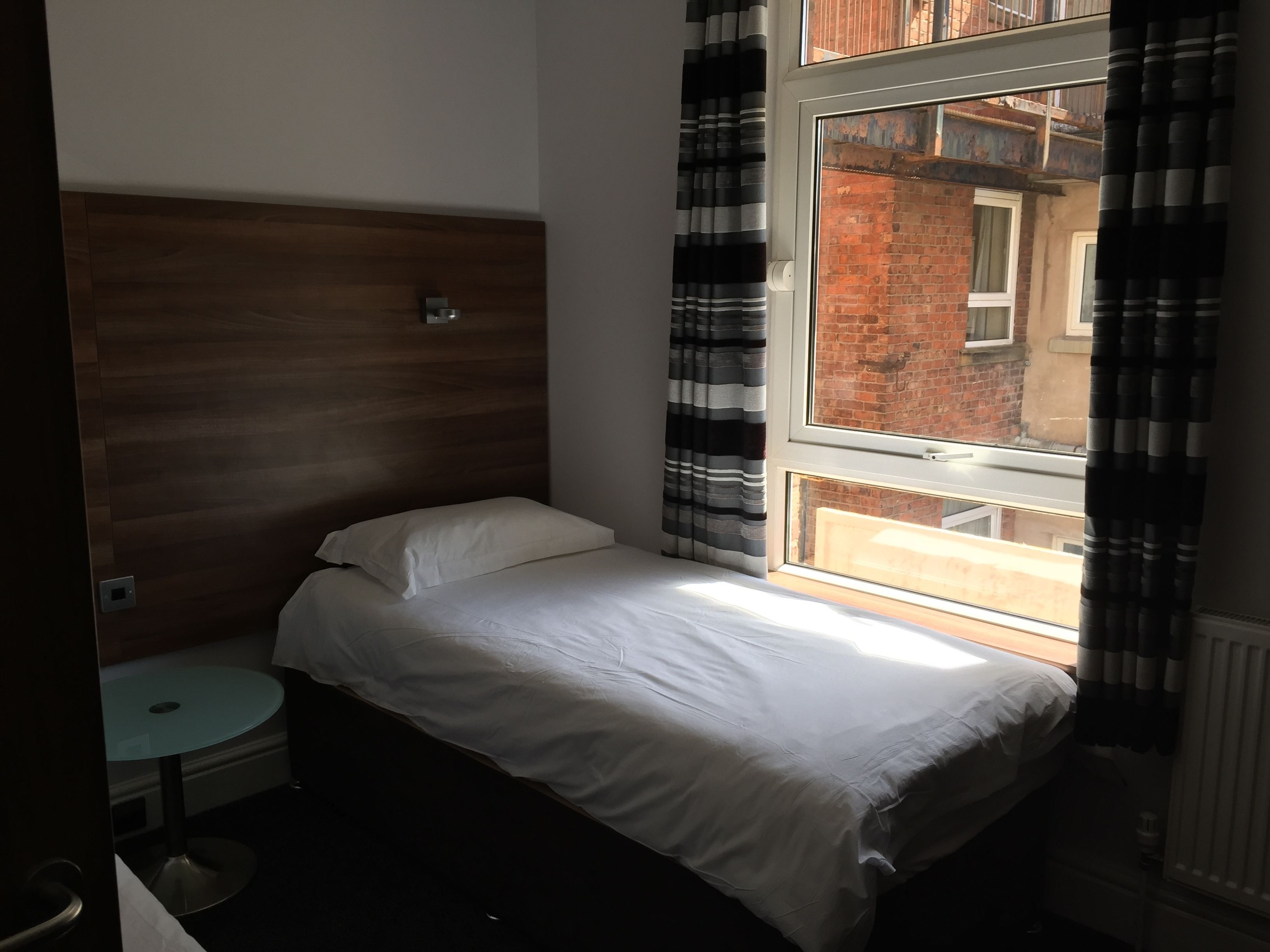 A bedroom with a bed, a small round table, and a window with curtains.
