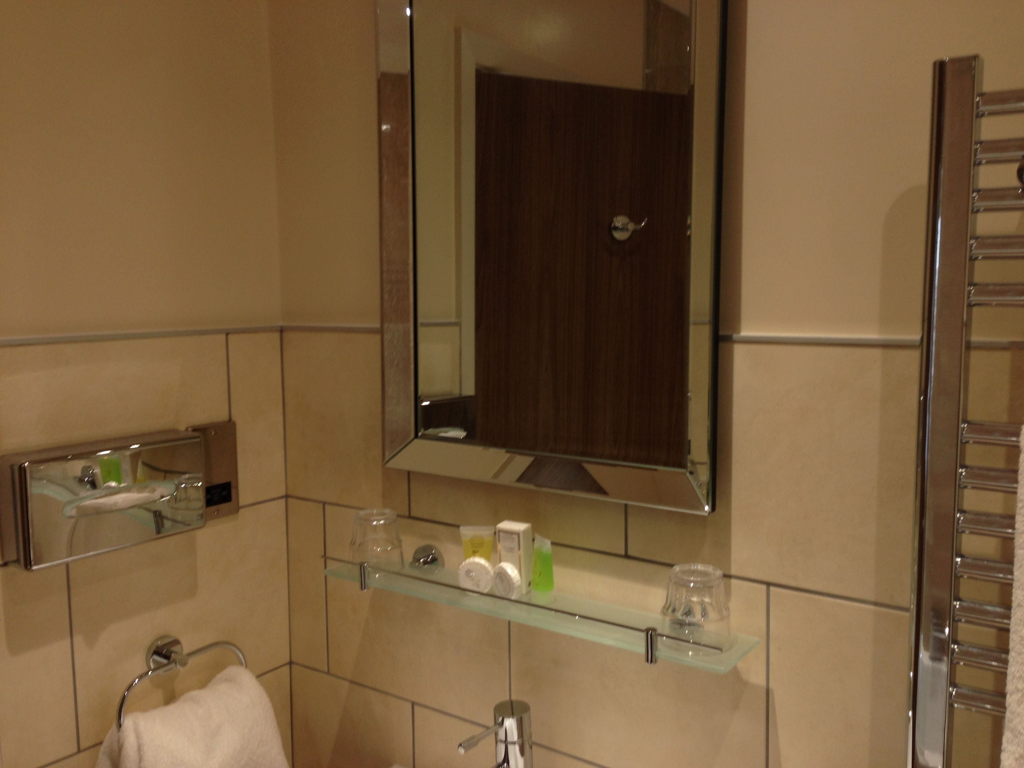 Un baño con un estante de vidrio que contiene artículos de aseo, un perchero y un espejo sobre un lavabo.