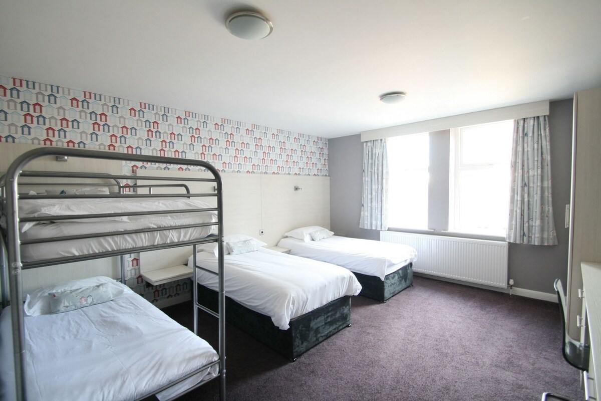 A dormitory room with bunk beds, a window with curtains, and a patterned wall.