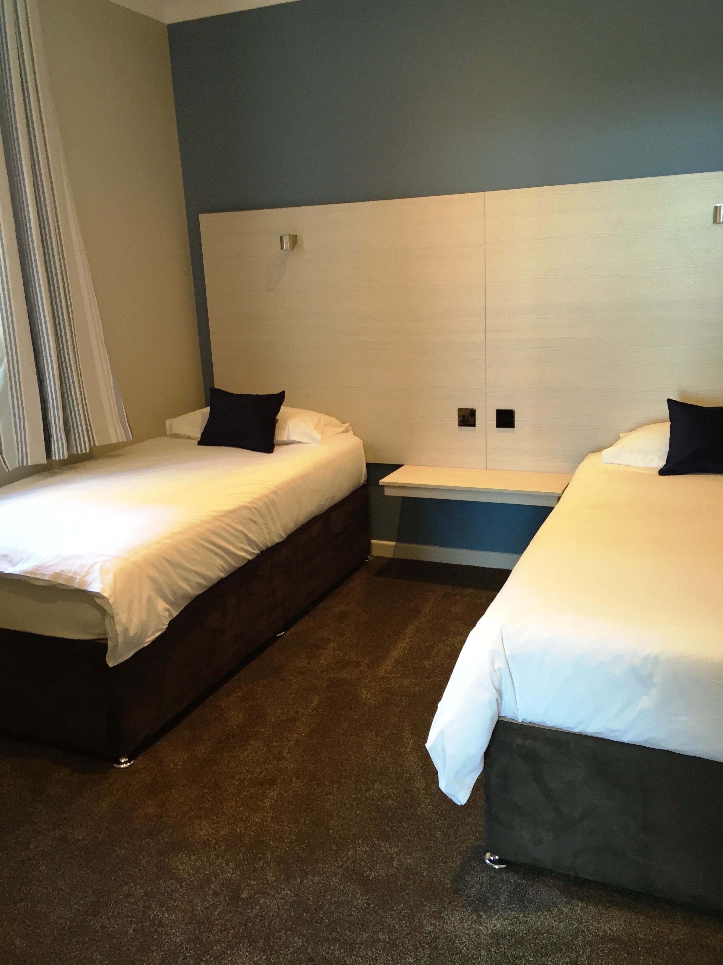 A hotel room with two beds, a large window with curtains, and a wooden headboard.