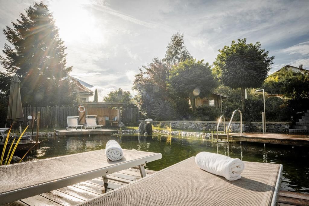 A serene outdoor pool area with lounge chairs, a wooden deck, and a stone wall.