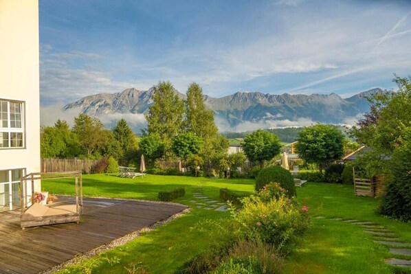 A garden with a wooden deck, a lawn, and a mountain backdrop. - Hotel Seppl (Mutters)